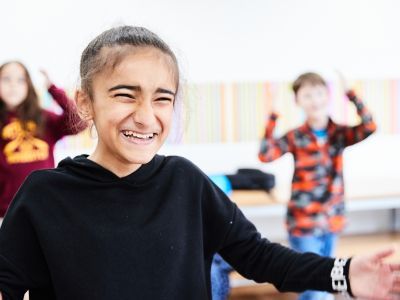 A young girl with black hair and a black jumper holds her hands out. She is laughing